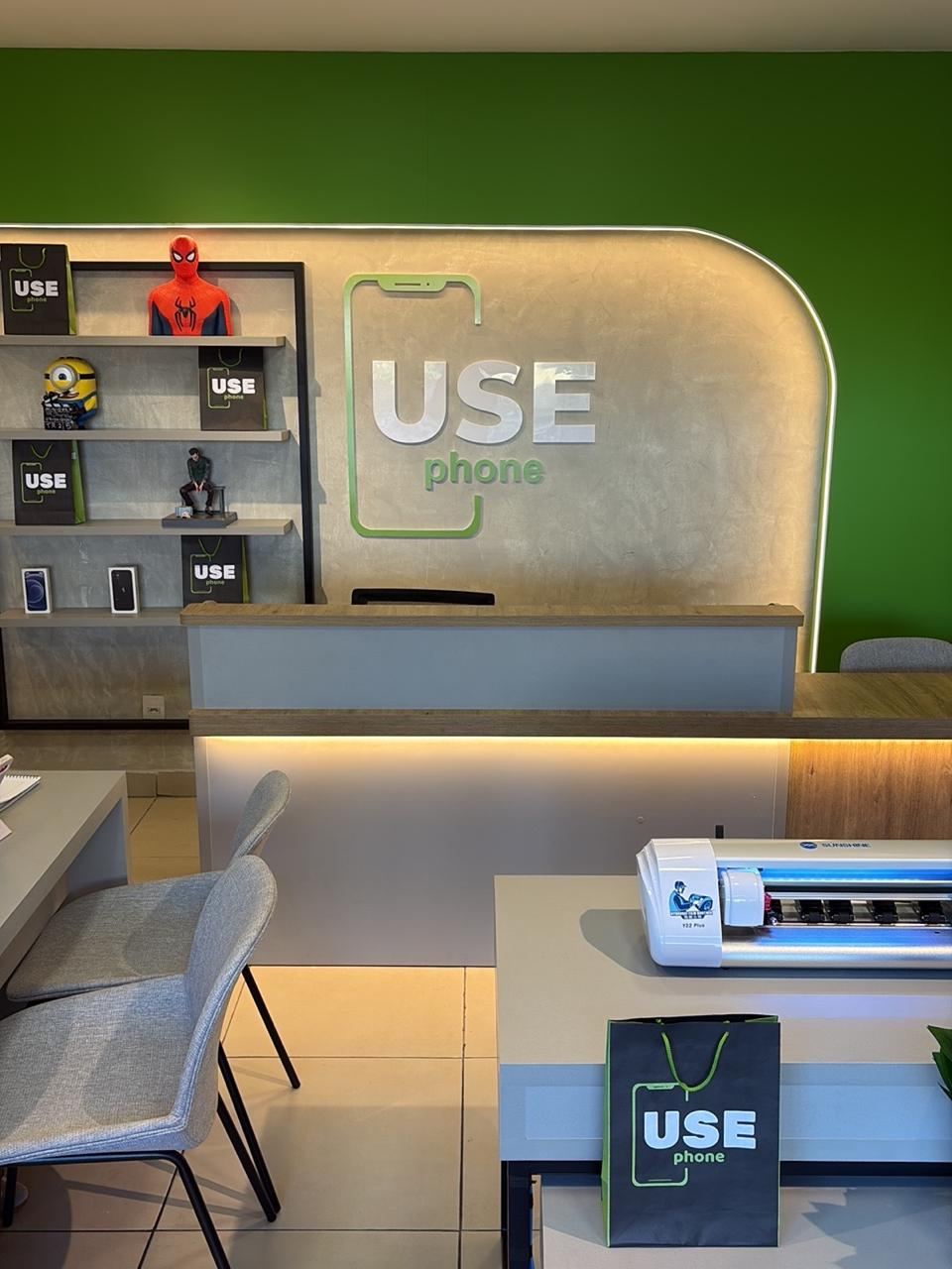 Balcão de atendimento com parede verde e o logo USE phone iluminado